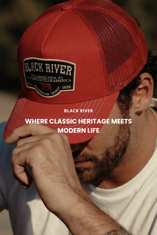 En mand sidder på en trækasse i et studie og bærer en klassisk brun cowboyhat i filt med bred skygge, en mørk denimskjorte og jeans.